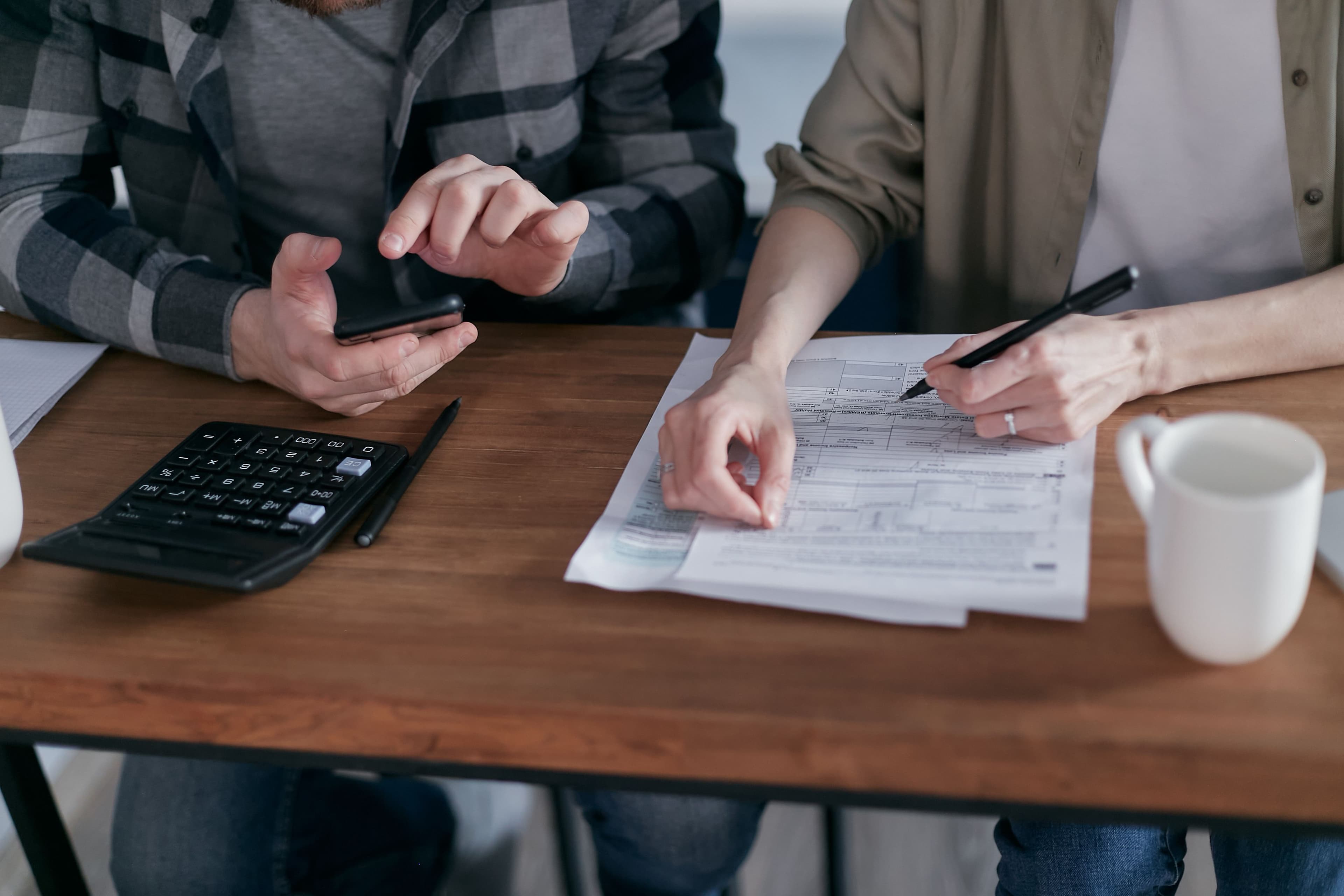 Manos revisando un formulario de impuestos 1040 sobre un escritorio, con una calculadora y un teléfono
